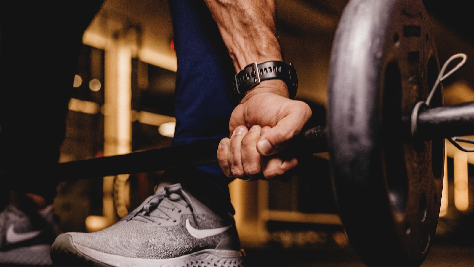 A person catching their breath beside a loaded barbell in a sunlit gym